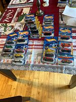 Lot of 23 Hot Wheels diecast toy cars arranged and packaged on a decorated table, each in original sealed blister cards, varying models and colors.