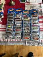 Photo showing 32 unopened Hot Wheels cars laid out on a table with different models and colors in original packaging.