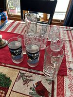 Overview of assorted 12 collectible glasses and mugs on table with holiday-themed cloth