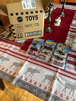Five Hot Wheels cars laid out on a table, each in sealed original packaging. The large Mattel Hot Wheels cardboard display box stands behind the cars. The photo shows the packaging condition and basic look of the cars.