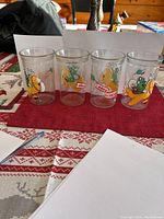 Four clear vintage Bick's drinking glasses with colorful vegetable cartoons on a table.