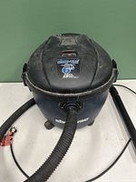 Front view of Shop Vac wet-dry vacuum showing the top lid, hose attachment, and branding label indicating 6.5 gallon capacity and 3.0 peak HP.