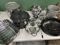 Full view of all cookware including pots, colanders, roasting pans and strainers on a table