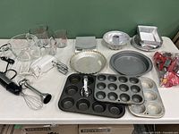 Full overview of all baking equipment items including measuring cups, mixers, pans, cookie cutters and food scale arranged on table.