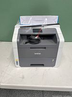 Front view of printer on table with power and USB cables coiled in output tray and paper stack on top