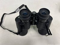 Top-down front view of black Bushnell binoculars showing lenses and eyepieces with rubber cups and attached neck strap.