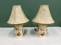 Pair of matching ceramic lamps with painted floral bases and cream fabric shades with bead fringe.