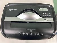 Top view capturing the Amazon Basics branding, control panel, and paper feed slot with shredder capacity and safety icons.