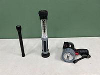 Three LED light tools: a slim black flashlight, a cylindrical LED worklight with transparent LED panel and rubber grip, and a large handheld spotlight flashlight with pistol grip.