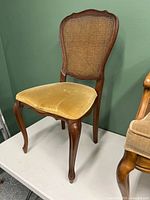 Single wooden side chair with caned back and mustard yellow upholstered seat, curved legs and carved wood frame, against green wall.