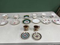 Full assortment of 6 teacups, 2 espresso cups, and 8 matching saucers arranged on a table, showing designs and condition.