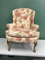 Front view of the floral upholstered wingback chair showing the floral fabric, cushion, and wooden legs.
