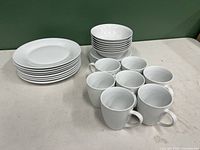 Photo showing stacks of white dinner plates, soup bowls, small plates, and 7 white teacups.
