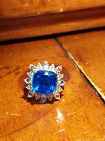 Front view of 925 sterling silver ring with a bright blue cushion-cut Caribbean Quartz surrounded by clear pear and round stones on wooden surface.
