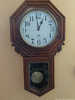 Front view of the octagonal antique regulator clock showing white dial with black Arabic numerals and brass bezel.