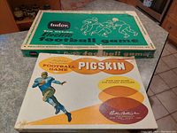 Photo showing original boxes of Tudor Electric Football Game (green box) and Parker Brothers Pigskin Football Game (white box) with vintage football illustrations