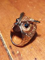 Side angle showing horned owl design with amber and clear multicolor crystals on head, black crystals for eyes, and gold tone stainless steel body with detailed feather texture.