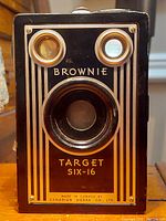 Front view of the Kodak Brownie Target Six-16 camera showing the lens, dual viewfinder windows, and gold geometric design with branding.
