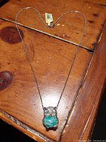 Photo of the owl pendant necklace laid flat on wooden surface showing full view of chain and pendant.