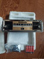 Front view of Wards Riverside AM Liftout Automobile Radio showing chrome panel, tuner dial, knobs, and treble/bass sliders, with original styrofoam packaging and accessory package including mounting hardware and batteries.