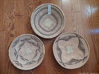 Photo displaying all three handwoven Sangwe baskets arranged on a wooden floor, showcasing distinct geometric patterns and natural earth tone colors.