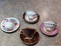 Four vintage English china tea cups with matching saucers displayed on a countertop showing front and sides.