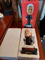 Wally Buono bobblehead figure displayed in original box and styrofoam packaging on wooden surface.