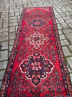 Full view of the semi-antique Persian wool runner on stone pavement, showing red background and four central medallions with intricate floral and geometric patterning.