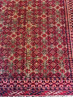 Close-up of intricate geometric diamond pattern in red, black, and cream on the wool rug.