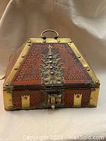 Front side of antique wooden jewelry chest box showing carved wood, brass lock plate, studs, and handle.