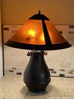 Full view of the lamp showing the dark metal base and warm amber Arts & Crafts style shade illuminated.