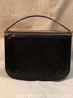 Front view of black clutch purse showing textured leather and gold-tone handle and frame.