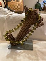 Overall view of heavy large tribal necklace draped over a rustic wooden display stand against a neutral background. Shows translucent greenish-yellow large glass beads of irregular shape and an ornate silk ball bead.