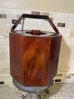 Front view of the ice bucket showing hexagonal dark brown acrylic with wood grain pattern, lid on, and handle up.