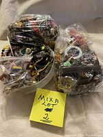 Photo showing multiple plastic bags and a container filled with assorted vintage jewelry items, including necklaces, bracelets, earrings, and brooches.