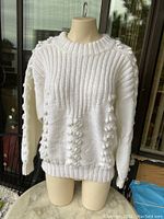 Front view of the cream wool sweater on mannequin, showing ribbed neck and bobble knit pattern.