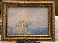 Full front view of framed signed watercolour painting depicting a large sailing ship and smaller boats with calm water and subtle clouds, with signature visible lower right.