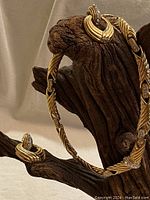 Gold-tone twisted rope design necklace and matching earrings displayed on a wooden stand, showing overall style and crystal embellishments.