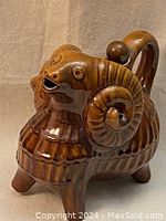 Front view of brown ceramic ram decanter showing detailed curved horns and glossy finish.