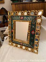 Front angled view showing gilded frame, colorful cloisonne hand-painted design, and multiple small mirror accents around the border.