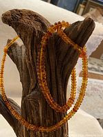 Front and side view of the necklace draped on a wooden display stand showing translucent amber beads of graduated size and color from light yellow to darker honey.