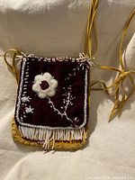 Front view of the vintage indigenous beaded cross body bag showing maroon velvet flap with white flower beadwork and fringe beaded edges, and yellow leather body and strap.