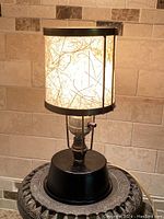 Full view of vintage miniature lamp lit on a textured tile background showing fibrous shade and metal base