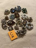 Top view of all 16 vintage jewelry pieces showing mixed brooches and pins with rhinestones, white beads, and assorted colors.