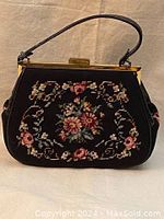 Front view of vintage black needlepoint handbag with floral embroidery, leather handle and brass clasp closure.