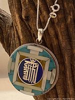 Close-up of front of the pendant showing intricate silver Tibetan script inset in lapis lazuli and bordered by turquoise and mother-of-pearl inlays.