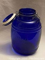Front view showing vintage cobalt blue glass jar with open wire clamp lid and embossed "COOKIES"