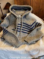 Gray wool hoodie with blue stripes lying flat on a white cloth, showing front side and hood with drawstrings.
