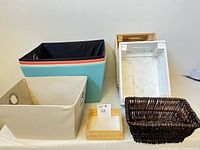 Photo of six storage bins: four large fabric bins in various colors, one tan fabric bin, two white wooden crate bins, one dark wicker basket, and one small wood tray