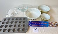 All items in the lot displayed on a white surface including Pyrex mixing bowls, clear glass bowls, mini muffin pan, and Reynolds parchment paper